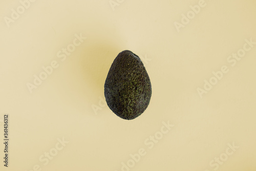 photo of a whole avocado on a pastel yellow background with a black  brown and green skin