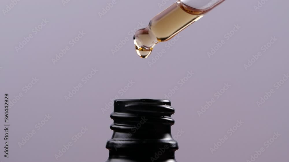 Essential oil dropping from glass dropper into bottle in slow motion