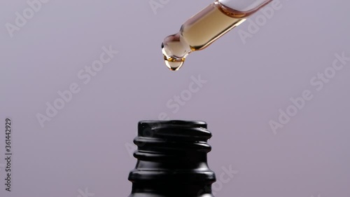 Essential oil dropping from glass dropper into bottle in slow motion