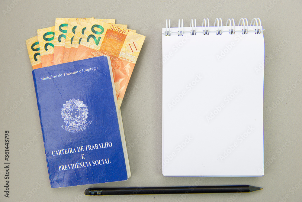 Top view of working card with money bills inside next to a notepad on blank background. Translate: Ministry of Labor and Employment - Employment and Social Security Card.