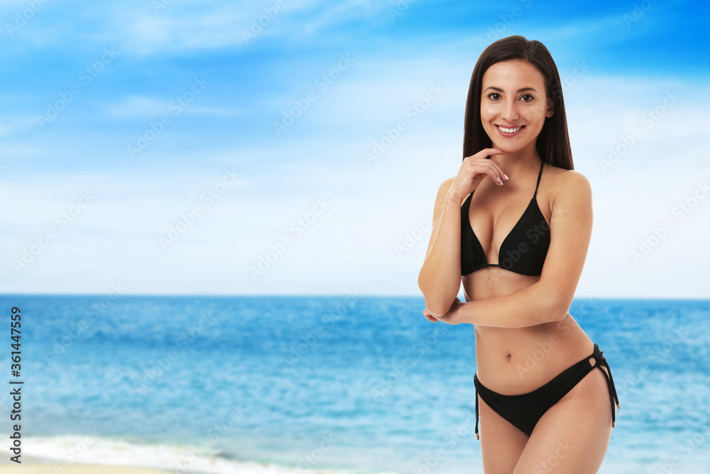 Pretty sexy woman with slim body in stylish black bikini near ocean on sunny day, space for text