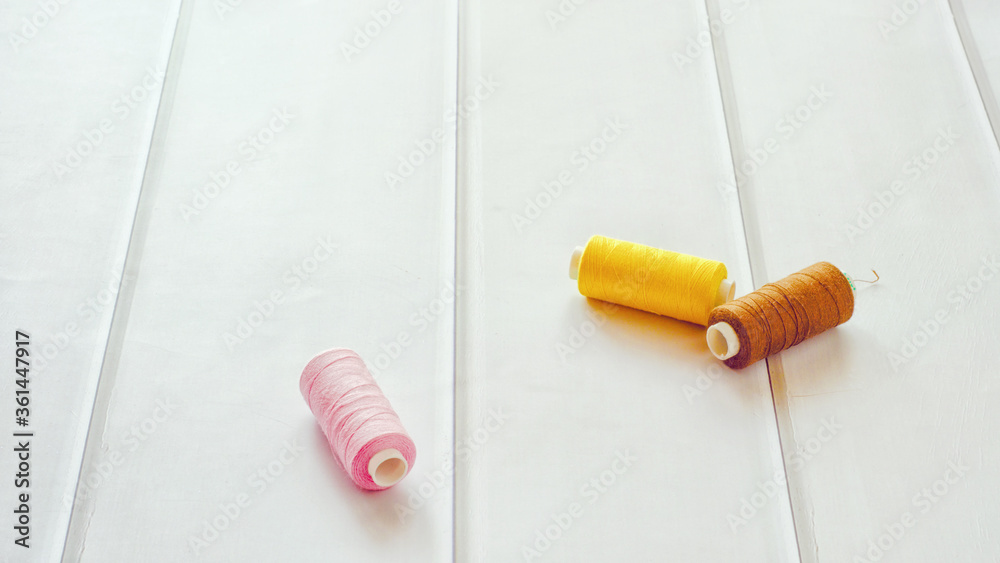 Naklejka premium Three reels of threads lie on a table of light wood.