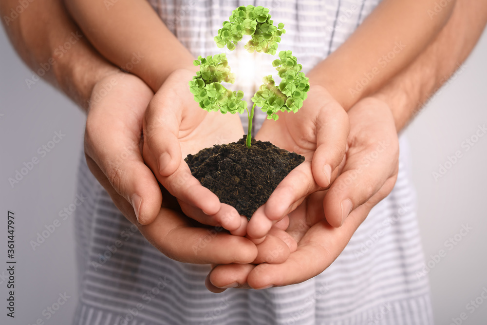 Family holding fertile soil in hands together and recycling symbol, closeup Family holding fertile soil in hands together and recycling symbol, closeup