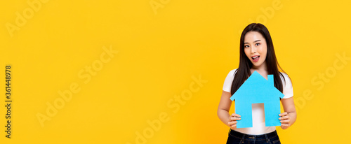 Young beautiful Asian woman holding new house model cutout isolated on colorful yellow banner background with copy space