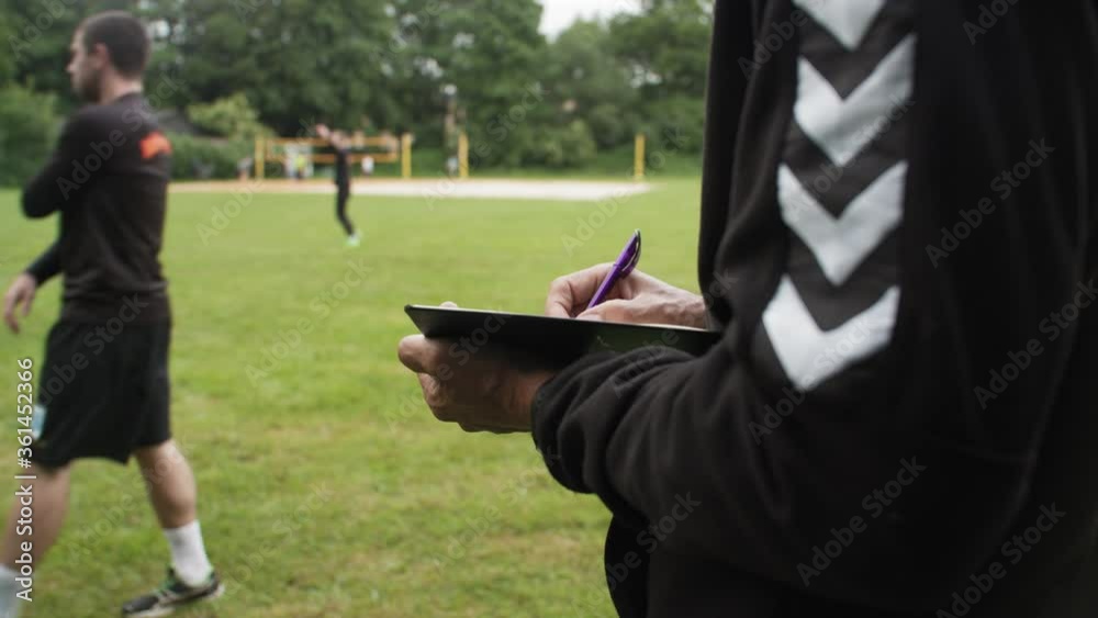 Scout writing notes in outdoor football practice. athletes warming up and running on grass. soccer game