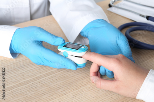 Doctor examining patient with modern fingertip pulse oximeter at wooden table  closeup
