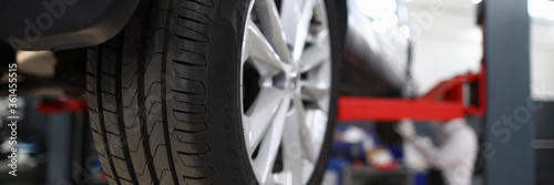 Close-up view of car all-season tire with aluminum rim. Mechanical lift for vehicle. Automobile service center or workshop concept. Professional auto maintenance photo
