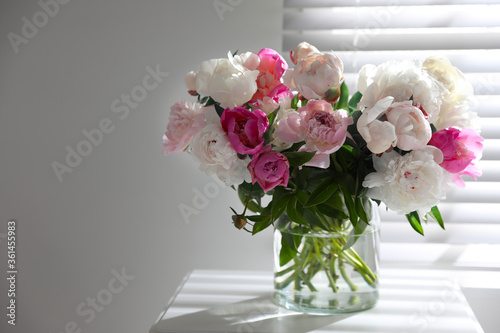 Beautiful peonies in vase on table near window indoors. Space for text