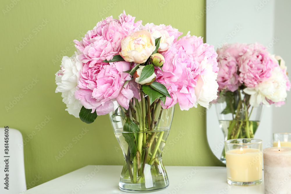 Beautiful peonies and candles on white dressing table near green wall