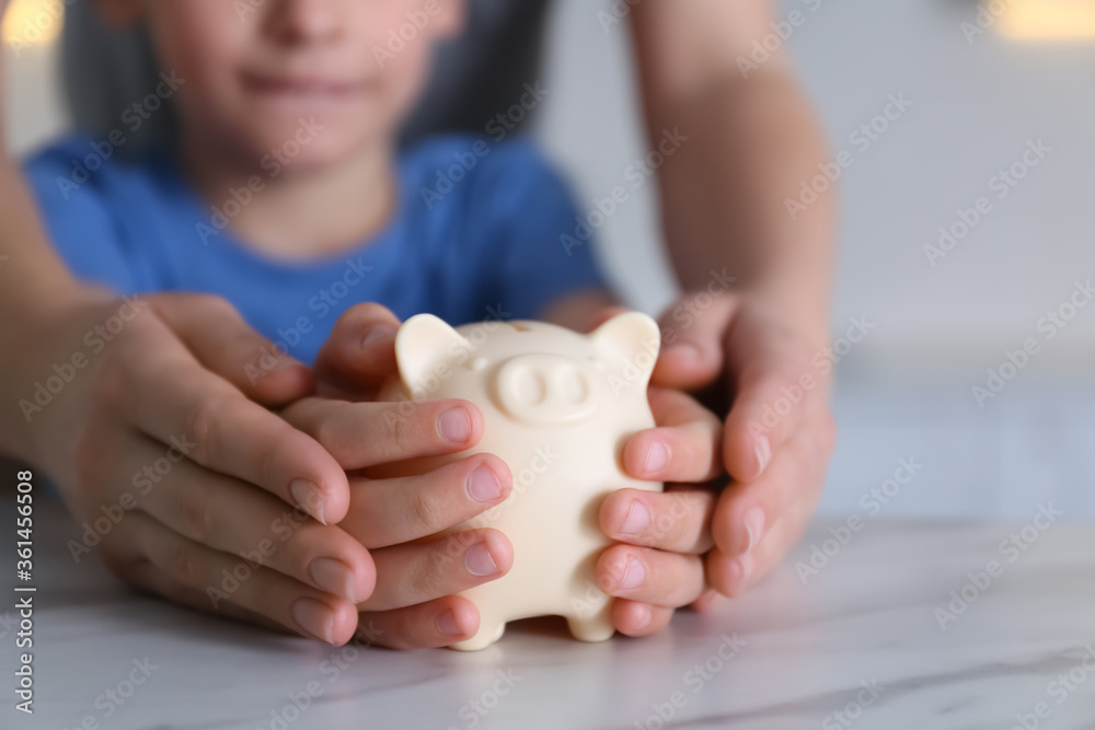 Mother and son with piggy bank at marble table indoors, closeup Mother and son with piggy bank at marble table indoors, closeup