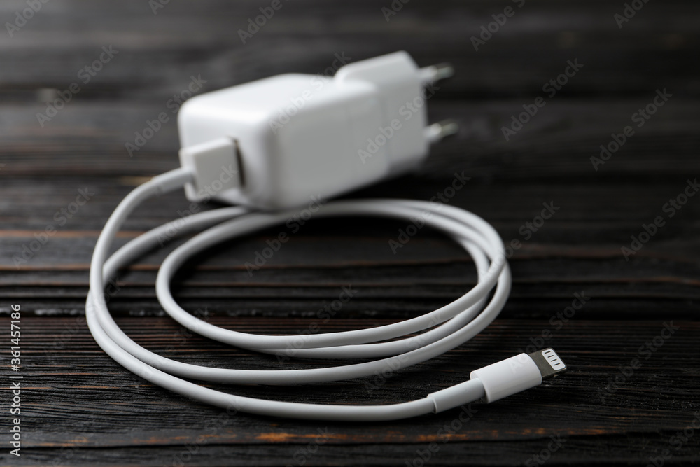 White charging cable and adapter on black wooden table White charging cable and adapter on black wooden table