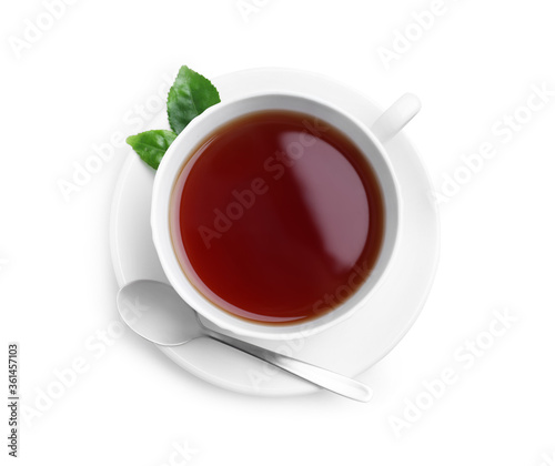 Cup of aromatic black tea, spoon and green leaves on white background, top view