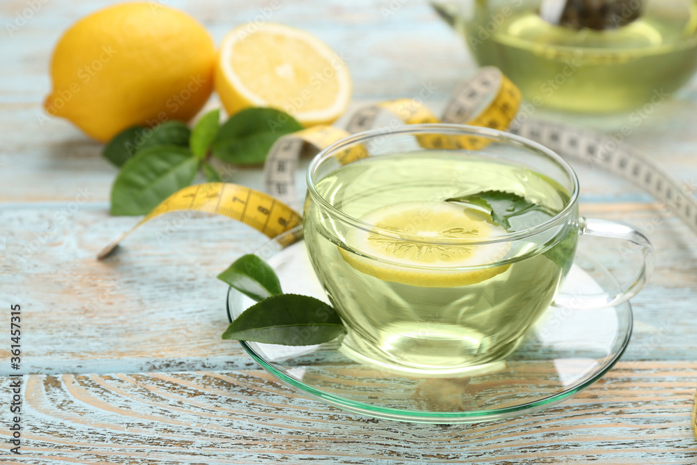 Glass cup of diet herbal tea with green leaves and lemon on wooden table Glass cup of diet herbal tea with green leaves and lemon on wooden table