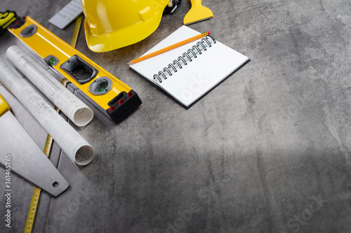 Contractor concept. Tool kit of the contractor: yellow hardhat, libella, hand saw. Plans and notebook on the gray tiles background. © zolnierek