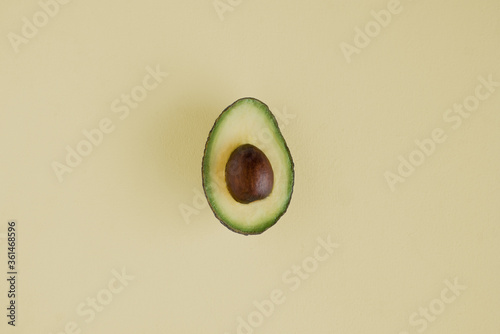 photo of half an avocado on a soft yellow background with  yellow and green flesh and a brown stone