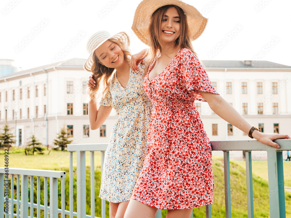 Two young beautiful smiling hipster girls in trendy summer sundress.Sexy carefree women posing on the street background in hats. Positive models having fun and hugging Two young beautiful smiling hipster girls in trendy summer sundress.Sexy carefree women posing on the street background in hats. Positive models having fun and hugging