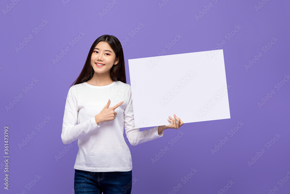 Waist up portrait of Smiling cheerful Asian woman pointing hand to blank paper board isolated on purple background Waist up portrait of Smiling cheerful Asian woman pointing hand to blank paper board isolated on purple background