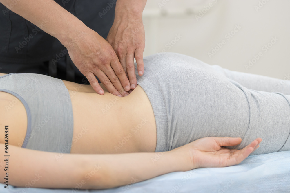Young woman having osteopathy treatment - giving a massage on the loin Young woman having osteopathy treatment - giving a massage on the loin