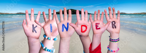 Children Hands Building Colorful German Word Kinder Means Kids. Ocean And Beach As Background