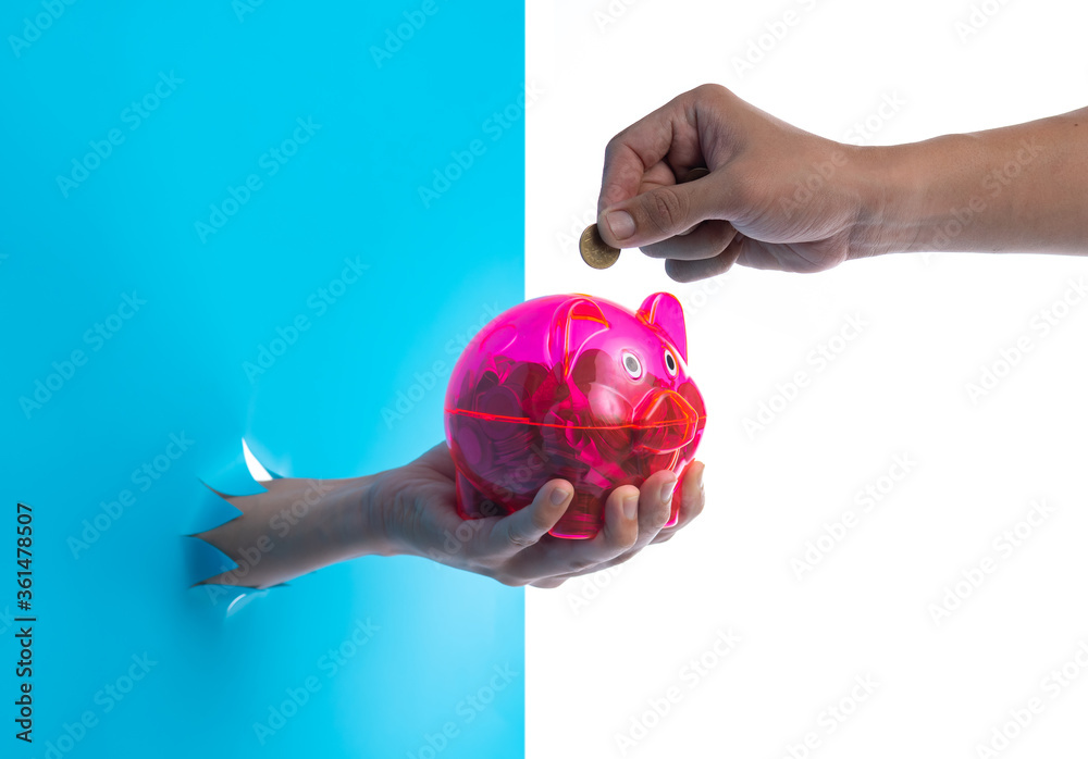 Hand holding a red piggy bank through the torn blue plastic background Hand holding a red piggy bank through the torn blue plastic background