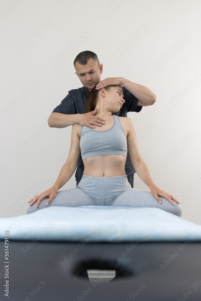Chiropractic treatment - young woman sitting on the couch and the doctor working with her neck - turning the head to the side Chiropractic treatment - young woman sitting on the couch and the doctor working with her neck - turning the head to the side