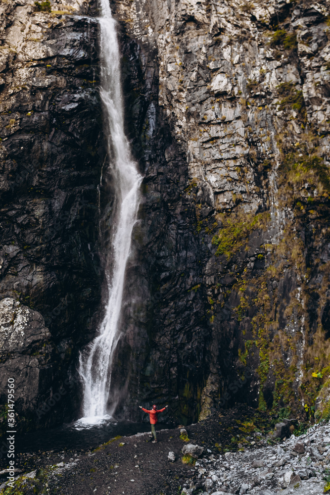 Obraz premium noise effect, selective focus: miniature tourist dressed in a bright colored raincoat that is contrastingly visible on a large scale background of a cliff with a waterfall