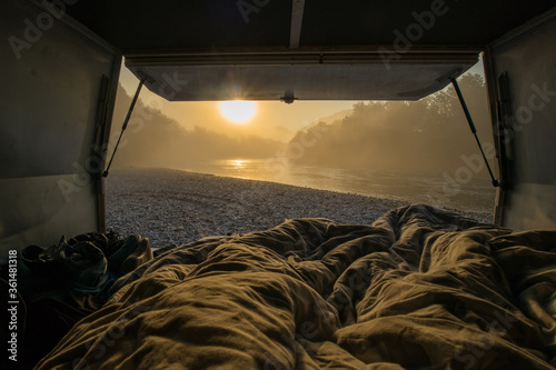 View from a bed in the vintage campervan parked on the shores of a river in early morning hours. Romantic overnight stay at a wild camping next to a river.