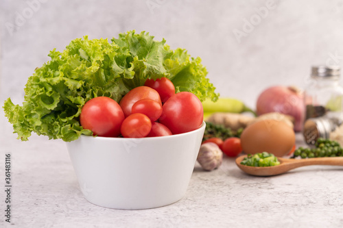 Lettuce and tomatoes in a white cup with sliced ​​onions and fresh peppers on the cement floor.
