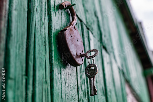 Old barn locks with keys hang on the painted green wood wall. Rusty metal device for closing doors.