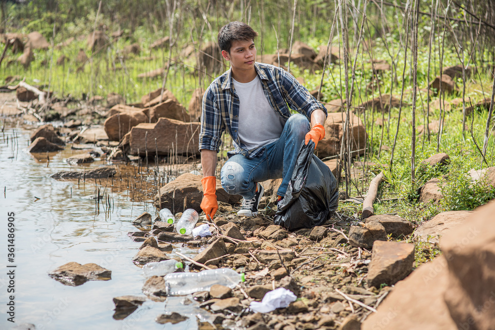A man wearing orange gloves collecting garbage in a black bag. A man wearing orange gloves collecting garbage in a black bag.