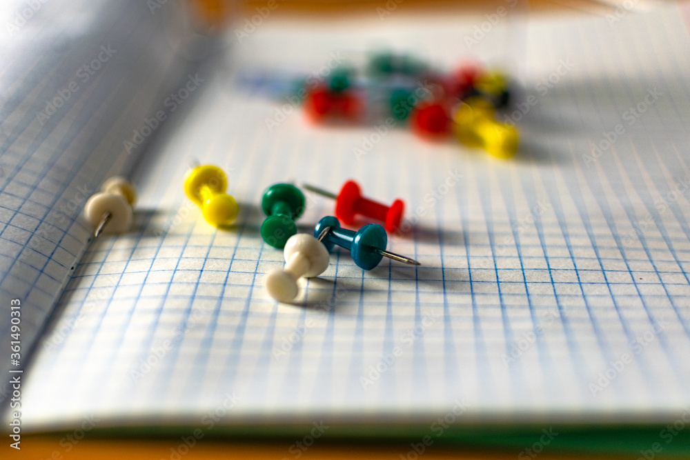 Colored small office buttons with different convenient protective hats, modern office details scattered on notebook leaves in a check Colored small office buttons with different convenient protective hats, modern office details scattered on notebook leaves in a check