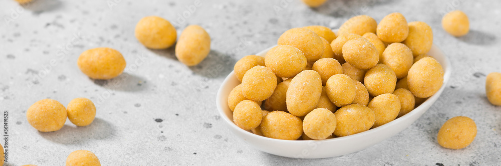 Fried peanuts in cheese sauce in a white bowl on a light gray table. Banner with space for text Fried peanuts in cheese sauce in a white bowl on a light gray table. Banner with space for text