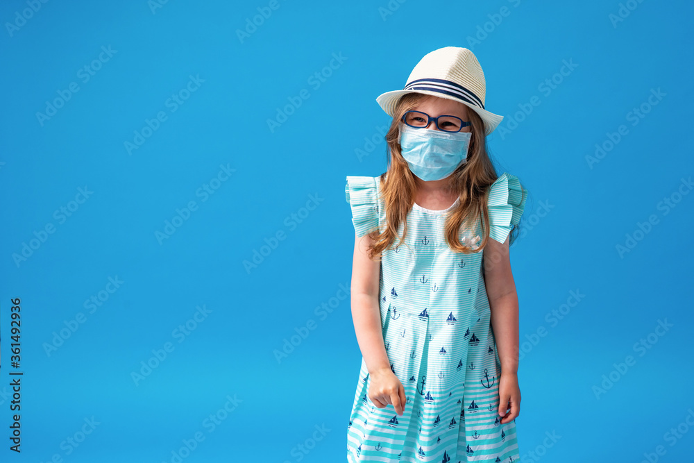 small girl in mask, glasses, hat and summer dress poses on a blue background. small girl in mask, glasses, hat and summer dress poses on a blue background.