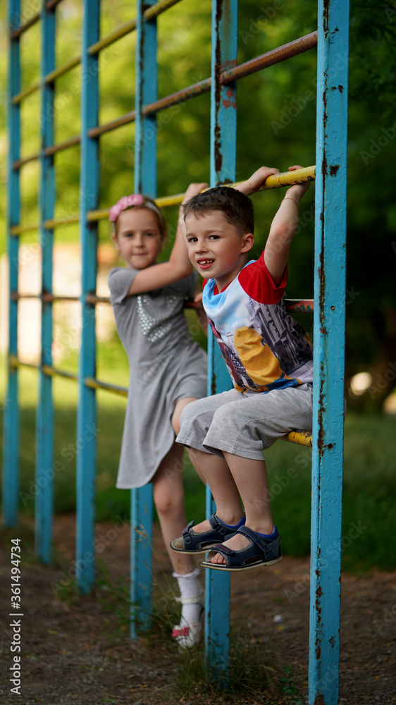 Fototapeta premium Cute little girl and boy hanging together on crossbar of sport staircase
