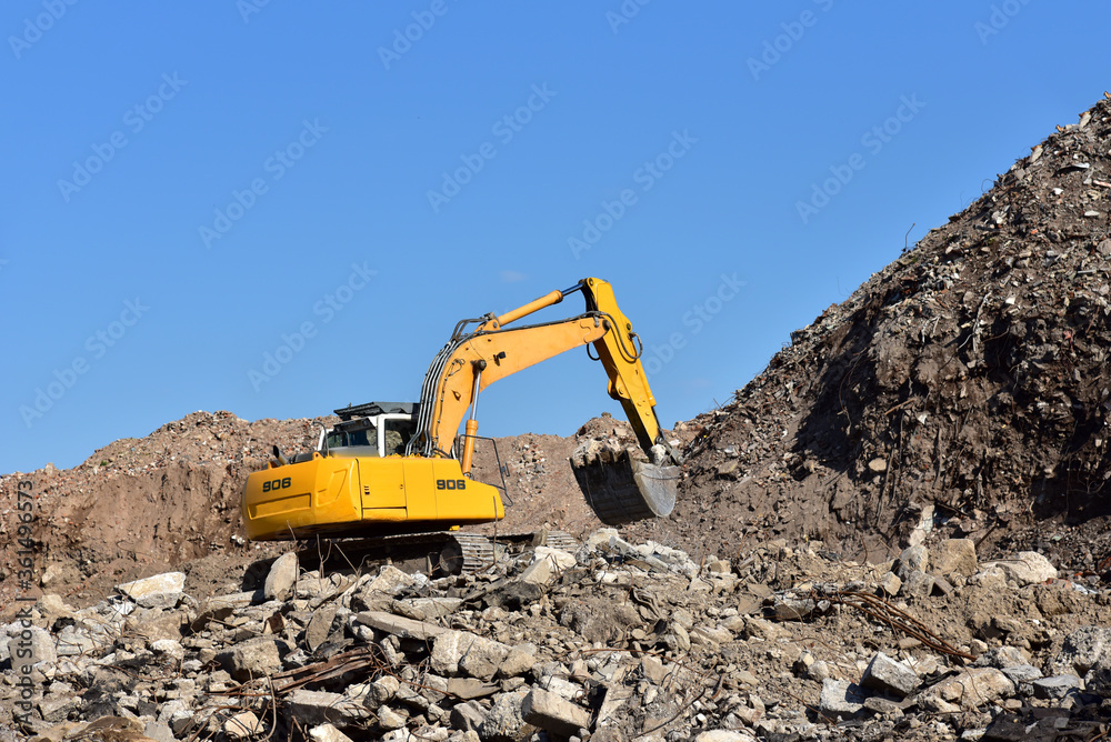 Yellow excavator at landfill for disposal of construction waste. Backhoe dig gravel at mining quarry on blue sky background. Recycling concrete and asphalt from demolition.