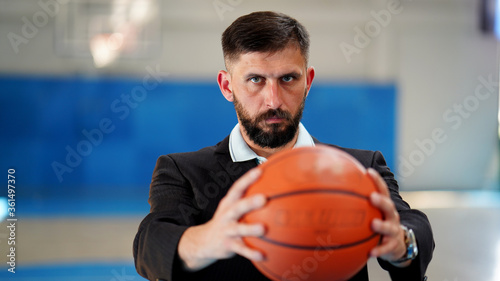 A young man with beard in a blazer with a basketball in hands