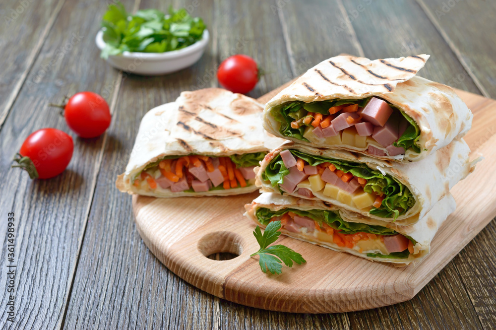 Lavash rolls with vegetables, ham and cheese. Tasty breakfast appetizer on a wooden board.