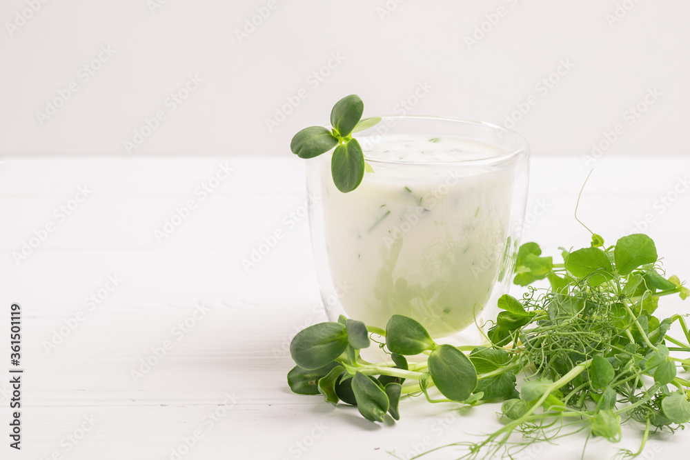 Green smoothie milkshake with the addition of fresh microgreen grass sprouts on white table. The concept vegetarianism. Green smoothie milkshake with the addition of fresh microgreen grass sprouts on white table. The concept vegetarianism.