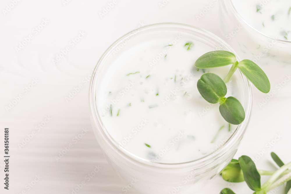 Green smoothie milkshake with the addition of fresh microgreen herb sprouts in a glass beaker on a white background. Green smoothie milkshake with the addition of fresh microgreen herb sprouts in a glass beaker on a white background.