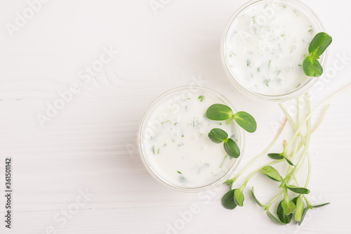 Green smoothie milkshake with the addition of fresh microgreen herb sprouts in a glass beaker on a white background.