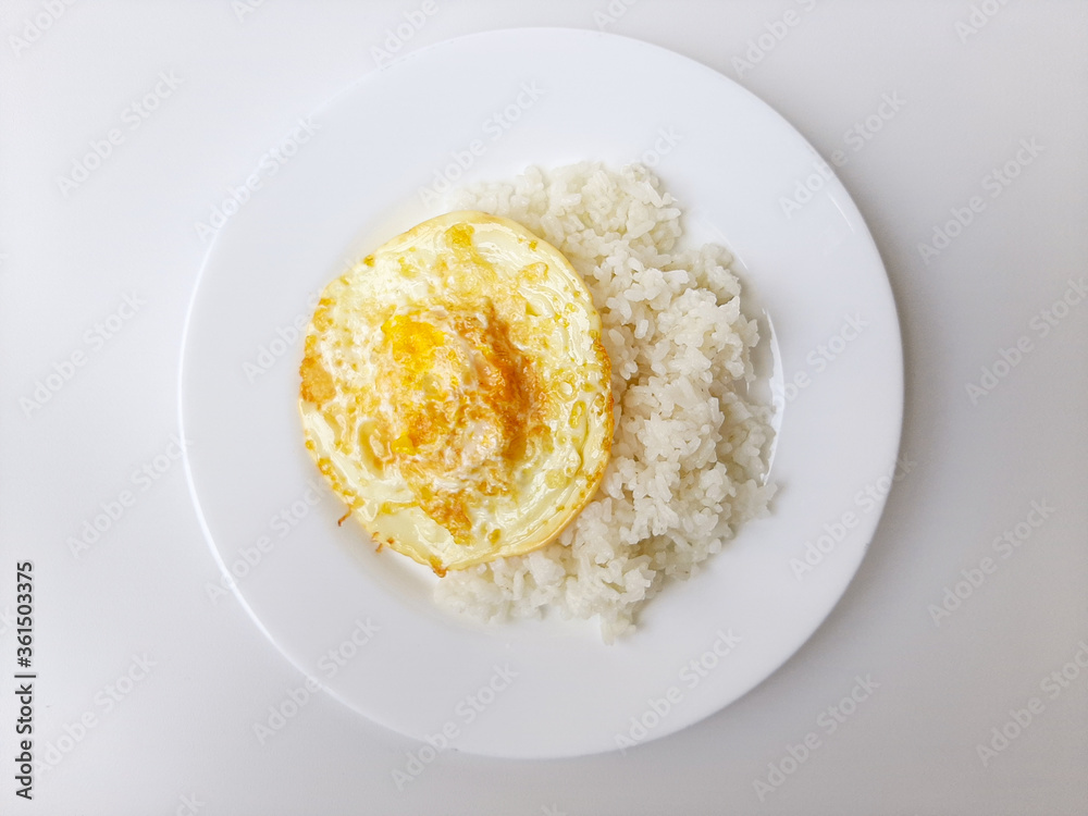 Fried egg or overcooked sunny side up, served with white rice, on a white plate, isolated in white background