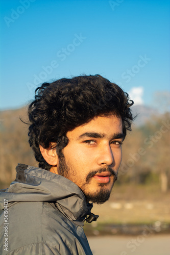 portrait of a handsome young man wearing a sports jacket taken in winter evening. Clear blue sky in background. Background is blurred. he has facial hairs and shabby hairstyle. sunlight on face.