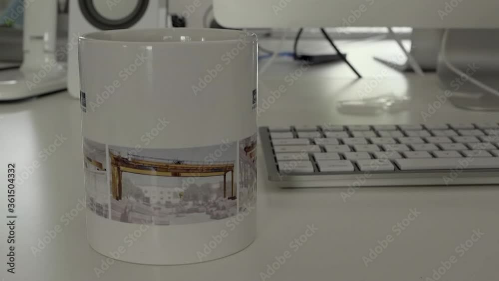 Coffee cup is being put on a table in front of a computer with keyboard