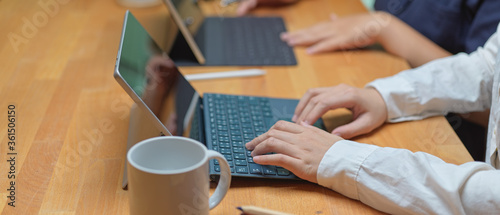 Female worker typing on digital tablet while sitting with her colleague at co working space