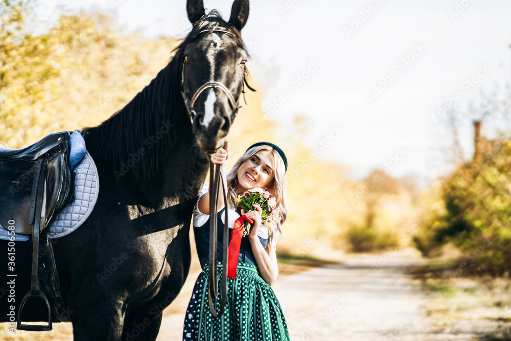 retty blonde in traditional dress  walking with big black horse outdoors