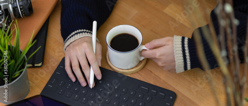 Female freelancer right hand typing on digital tablet keyboard and left hand holding coffee cup
