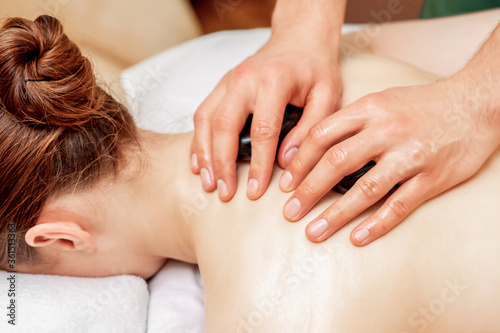 Hands of massage therapist doing back massage with massage stones on back of woman close up.