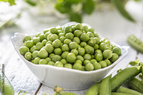 Green raw peas and pods in pocelain bow isolated on wooden table photo