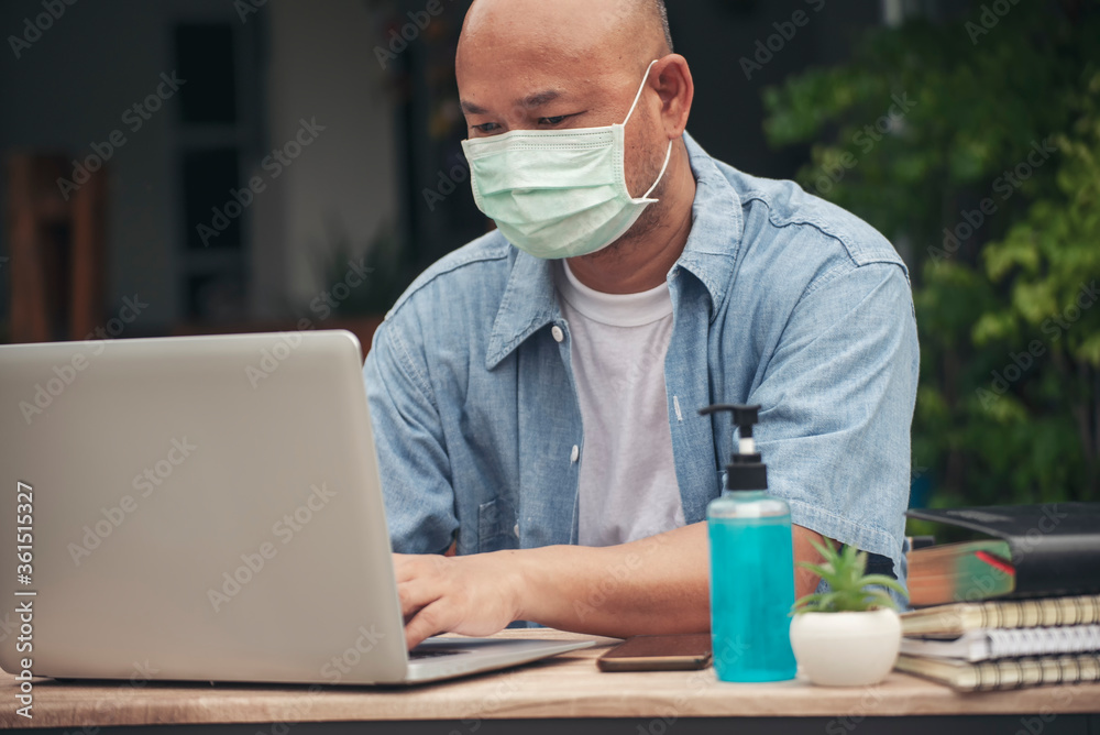 Businessman wear mask working online at the home office on the laptop. Asian young entrepreneur watching webinars during meeting vdo conference with team work.Technology concept Businessman wear mask working online at the home office on the laptop. Asian young entrepreneur watching webinars during meeting vdo conference with team work.Technology concept