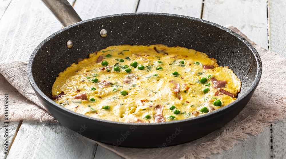 Omelette with prosciutto peas and herbs in ceramic pan on table